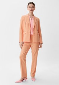 Pfaumpink maßgeschneiderter Anzug mit einem Zweiknopf-Blazer und geraden Hosen, kombiniert mit einer hellrosafarbenen Bluse und pinken Absatzmules.