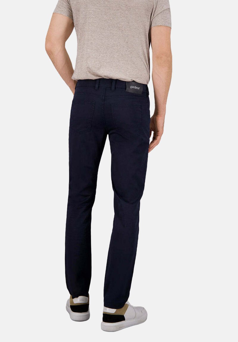 Pantalons bleu marine ajustés, en tissu doux, dotés de poches arrière et d'une étiquette à la taille. Portés avec des baskets blanches décontractées.