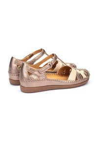 Dames sandalen met een metallic bronzen afwerking, crisscross banden, een platte zool en stiksels langs de randen.