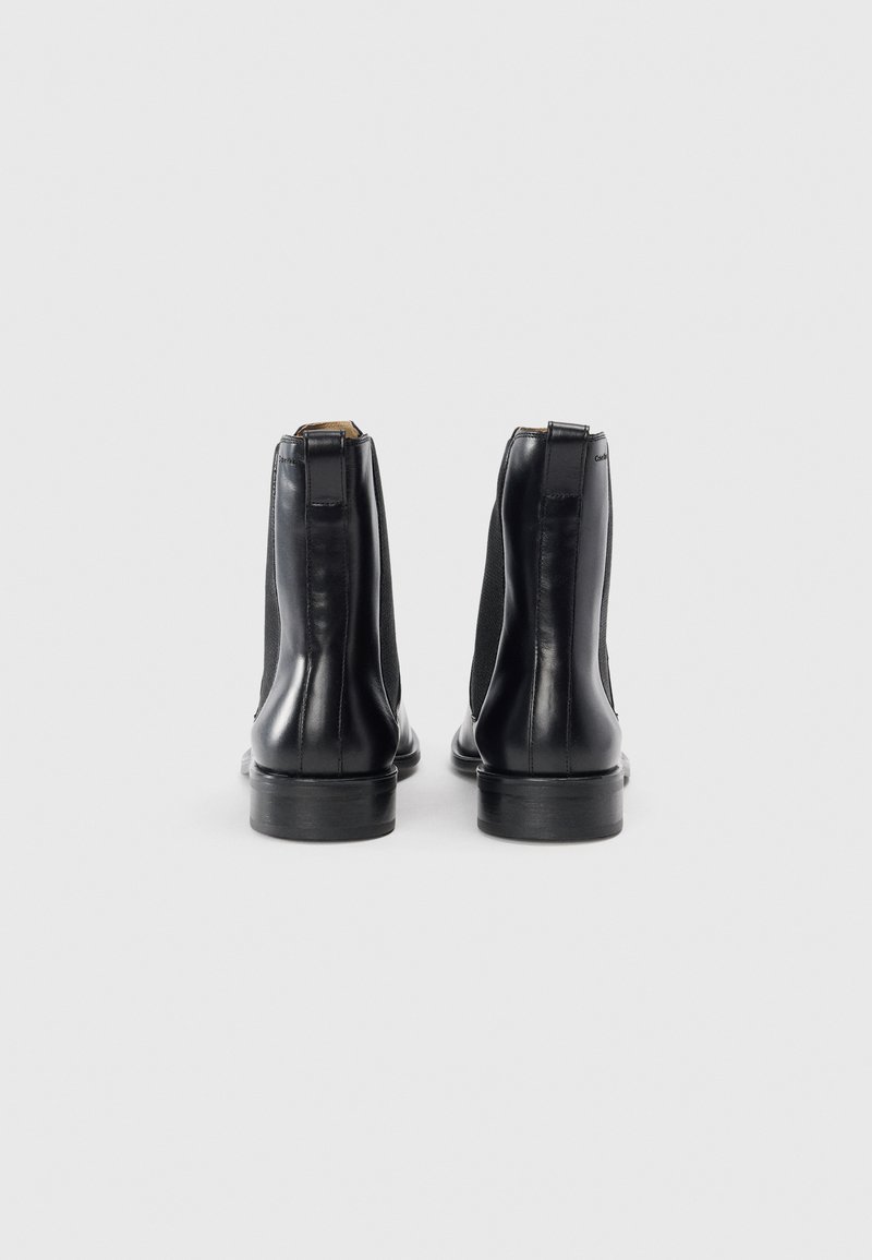 Bottines Chelsea en cuir noir avec côtés élastiques, texture lisse, bout arrondi et semelle en caoutchouc noir solide. Présente un onglet de talon renforcé.