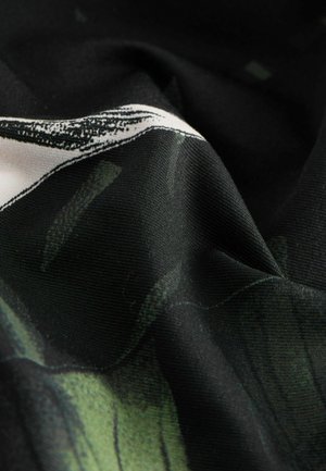 Primo piano di tessuto nero con disegno astratto stampato in verde e bianco, che mostra texture e pieghe.