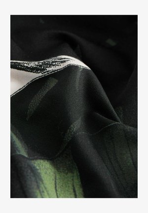 Zbliżenie czarnej tkaniny z zielonym i białym abstrakcyjnym nadrukiem, ukazujące fakturę i fałdy.