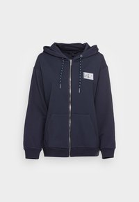 Sudadera con cremallera de color azul marino, con capucha, bolsillos frontales y un parche de logo en plata. Cuenta con cordones de contraste en azul y puños y dobladillo acanalados.