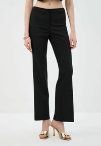 Black tailored trousers with a straight-leg design, flat front, and a smooth texture. Worn with metallic open-toe heels.
