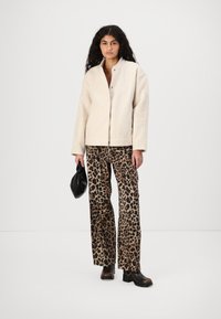 Cremfarbener, strukturierten Fleece-Jacke mit hohem Kragen und Druckknopfverschluss, kombiniert mit einer leopardgemusterten, weiten Hose und schwarzen Accessoires.