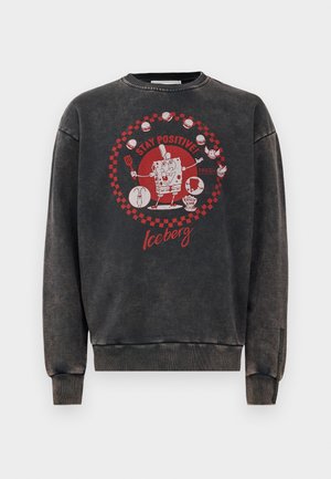 let sweatshirt i sort med en falmet finish, der har en rød grafik af en tegnefilmsfigur samt teksten "STAY POSITIVE" i et rundt design.