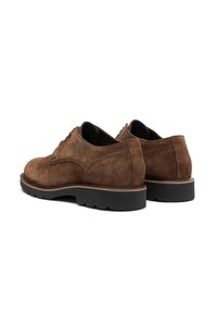 Une paire de chaussures en suede marron à lacets avec des semelles en caoutchouc noires, présentée de dos sur fond blanc.