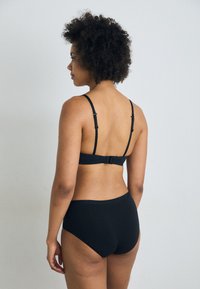 Ensemble de lingerie noir en tissu lisse et extensible. Le soutien-gorge possède des bretelles ajustables et une fermeture à agrafes, avec un bas taille mi-haute.