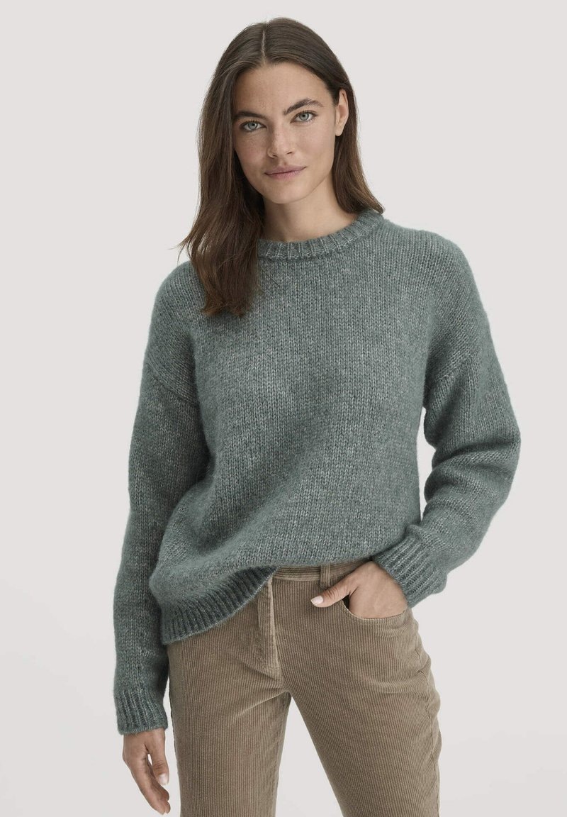 Grauer Strickpullover mit Rundhalsausschnitt und langen Ärmeln, mit texturiertem Finish und lockerer Passform. Kombiniert mit Cordhosen.