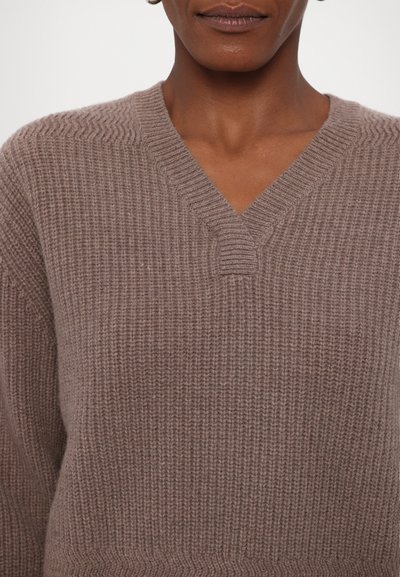 V-Ausschnitt Strickpullover in einem warmen Taupe. Verfügt über eine gerippte Textur und ein dezentes horizontales Muster. Weicher Stoff und lockere Passform.