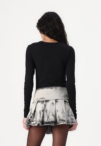 Un haut à manches longues noir associé à une jupe en jean courte plissée avec un motif tie-dye noir et gris, dotée d'une taille ajustée et d'un ourlet volanté.