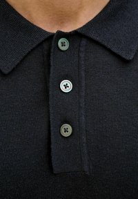 Svart polo skjorte med teksturert strikk, tre frontknapper med grønn nyanse og klassisk krage.