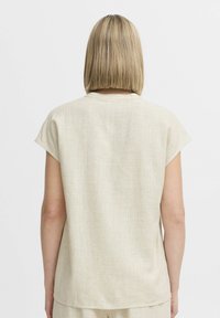 Top beige a maniche corte con una vestibilità morbida, caratterizzato da un tessuto leggermente testurizzato e un collo arrotondato, visto da dietro.