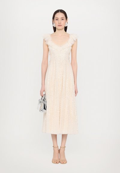 Beige mekko, jossa on paljetteja, V-pääntie, röyhelöillä varustetut olkapäät, laskostettu hammas, yhdistettynä hopeiseen käsilaukkuun ja nude-korkokenkiin. Silkkinen kankaan rakenne.