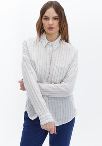 Lichtgewicht button-up shirt in crème met blauwe verticale strepen, voorzien van een klassieke kraag en een enkele borstzak. Lange mouwen met manchet.