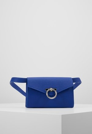 Niebieska skórzana saszetka z kopertową klapą i srebrnym zapięciem w formie pierścienia, prezentowana na białym piedestale na jednolitym szarym tle.