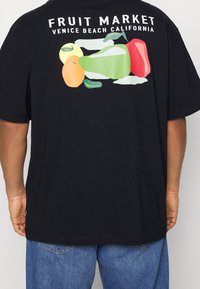 T-shirt nera con una grafica colorata di frutta e il testo "FRUIT MARKET VENICE BEACH CALIFORNIA" in bianco sulla schiena.