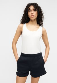 Haut blanc sans manches en tissu lisse, associé à un short noir à coupe décontractée avec une taille élastique et des poches latérales.