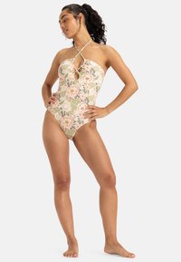 Bloemen eendelig badpak met halterhals, sleutelgatdetail en pastelkleuren. Bevat een mix van grote roze bloemen en groene bladeren.
