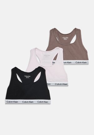 Tre reggiseni sportivi Calvin Klein racerback in nero, bianco e marrone con bande elastiche marchiate, disposti sovrapposti su uno sfondo semplice.