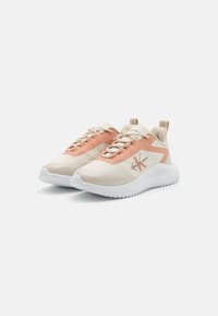 Chaussures de sport légères en beige et pêche avec un dessus en synthétique lisse, un collier rembourré et une semelle en caoutchouc blanc texturé.