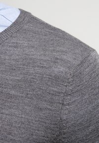 Grauer Strickpullover mit einem gerippten Ausschnitt und glatter Textur, der ein dezentes Muster im Stoff zeigt. Keine sichtbaren Logos oder Akzente.