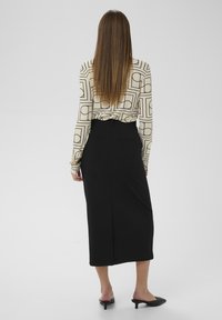 Čierna ceruzková sukňa s rázpírom vzadu, kombinovaná so vzorovanou krémovou blúzkou s geometrickými tvarmi v čiernej farbe. Hladká textúra s priliehavým strihom.