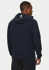 Felpa con cappuccio blu navy, in misto cotone, presenta una tasca a marsupio e un accento a righe sulla scollatura posteriore. Tessuto morbido, vestibilità rilassata.