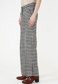 Pantalons taille haute à motif pied-de-poule noir et blanc avec une coupe droite, présentant un devant plat et des poches latérales.