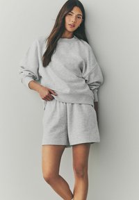 Grijze fleece sweatshirt met verlaagde schouders, gecombineerd met bijpassende grijze shorts. Zachte textuur, relaxte pasvorm, ribgebreide manchetten en tailleband.