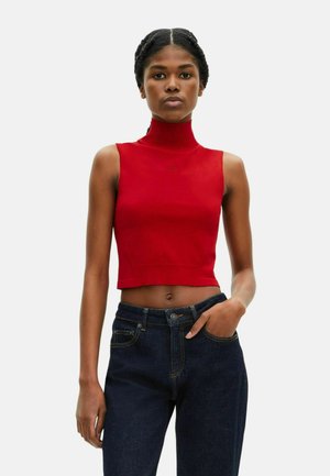 Top corto sin mangas de cuello alto en rojo, diseño ajustado, textura acanalada, con un logo en relieve en el pecho, combinado con unos jeans de mezclilla oscura de tiro alto.