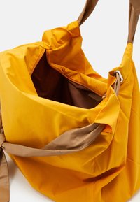 Duża torba tote w intensywnym żółtym kolorze z gładkiego materiału, z brązowym wnętrzem i kontrastującymi brązowymi uchwytami.