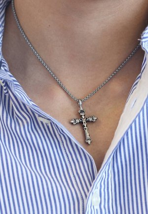Silver-tone cross pendant on a chain, featuring intricate designs and floral accents, worn over a blue and white striped shirt.