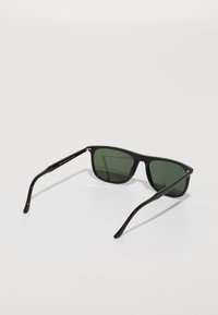 Ochelari de soare negri cu lentile verzi, cadru rectangular, finisaj lucios și brațe subțiri cu branding subtil și accente metalice.