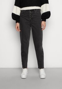 High-waisted black denim jeans with a straight leg, button fly closure, and subtle fading. Paired with white sneakers on a gray background.