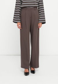 Brown high-waisted wide-leg trousers with pleats, made from smooth fabric. Paired with a striped long-sleeve top and black pointed shoes.
