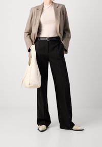Béžový pruhovaný blazer, krémový žebrovaný top, černé kalhoty a bílé ploché boty s cvočky. Drží bílou kabelku. Jednoduchý design, strukturovaná tkanina.