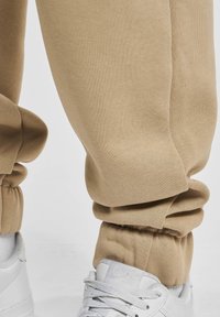 Beige joggings met een taps toelopend ontwerp en geribbelde boorden, gecombineerd met witte sneakers met veters en een gestructureerd oppervlak.