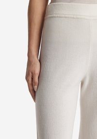 Vita, texturerade byxor med rak passform. Den höga midjan är snyggt sytt, med en hand som vilar på lårområdet.