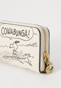 Portefeuille en cuir blanc avec un design de dessin animé représentant un personnage sur une planche de surf avec le texte "COWABUNGA !". Fermeture éclair et accents en métal doré.