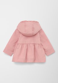 Vaaleanpunainen vedenpitävä takki, jossa on ryppyhuppu, pitkät hihat ja liehuva helma. Tasainen pinta ja yksinkertainen muotoilu, ei näkyviä kiinnityksiä.