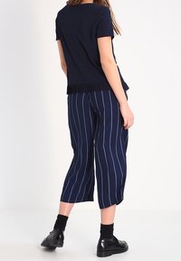 Navy short-sleeve top with a pleated hem, paired with navy cropped pants featuring white vertical stripes. Black socks and shoes complete the outfit.