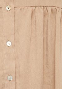 Camicia button-up beige chiaro in tessuto testurizzato, con delicate pieghe e bottoni in madreperla sul davanti.