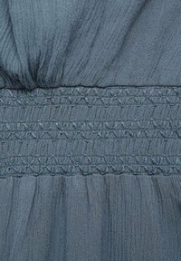 Țesătură texturată albastră cu pliuri adunate și detalii de broderie orizontală, creând o apariție moale și fluidă.