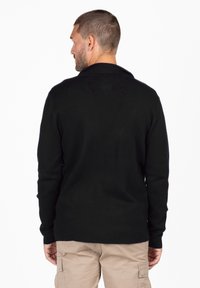 Pullover a maglia nera con maniche lunghe, colletto pieghevole e vestibilità rilassata, caratterizzato da una consistenza liscia e senza motivi visibili.