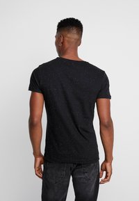 Camiseta negra con mangas cortas y cuello redondo, que presenta un patrón moteado. La tela parece suave y ligeramente texturizada.