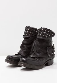 Botas negras de cuero hasta el tobillo con un diseño holgado, que cuentan con un puño con tachuelas, herrajes metálicos y un tacón grueso y resistente.