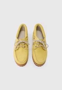 Κίτρινα παπούτσια από σουέντ με στρογγυλή μύτη, σχέδιο με κορδόνια, ανοιχτογκρι κορδόνια και καφέ ελαστική σόλα. Λείο υφή και διακοσμητικές ραφές.