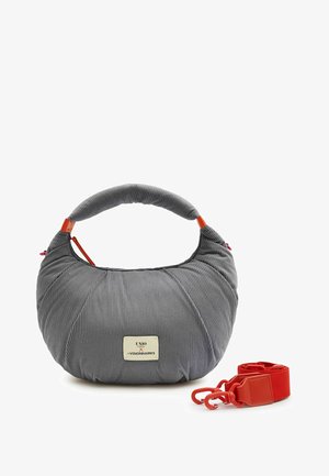 Gray ribbed fabric handbag with short padded handle, rectangular front label, and detachable red strap with clasps beside it.