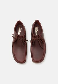Chaussures en cuir marron avec une forme arrondie, un design à lacets et des semelles intérieures rembourrées. Présente des coutures visibles et une surface légèrement texturée.
